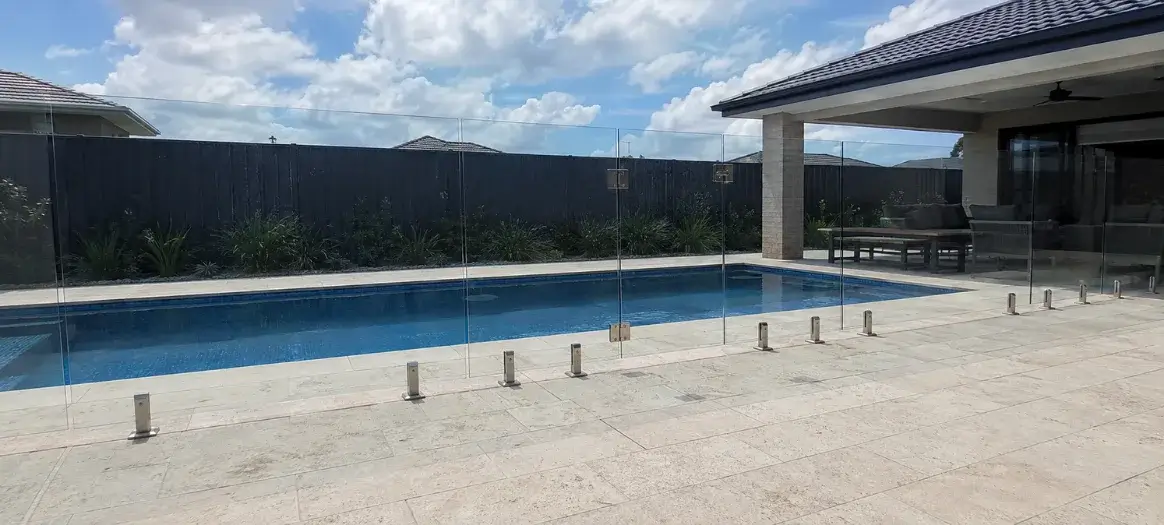 A clear glass pool fence surrounding a backyard swimming pool in Newtown